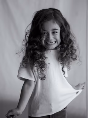 Black and white portrait of a curly-haired girl smiling broadly